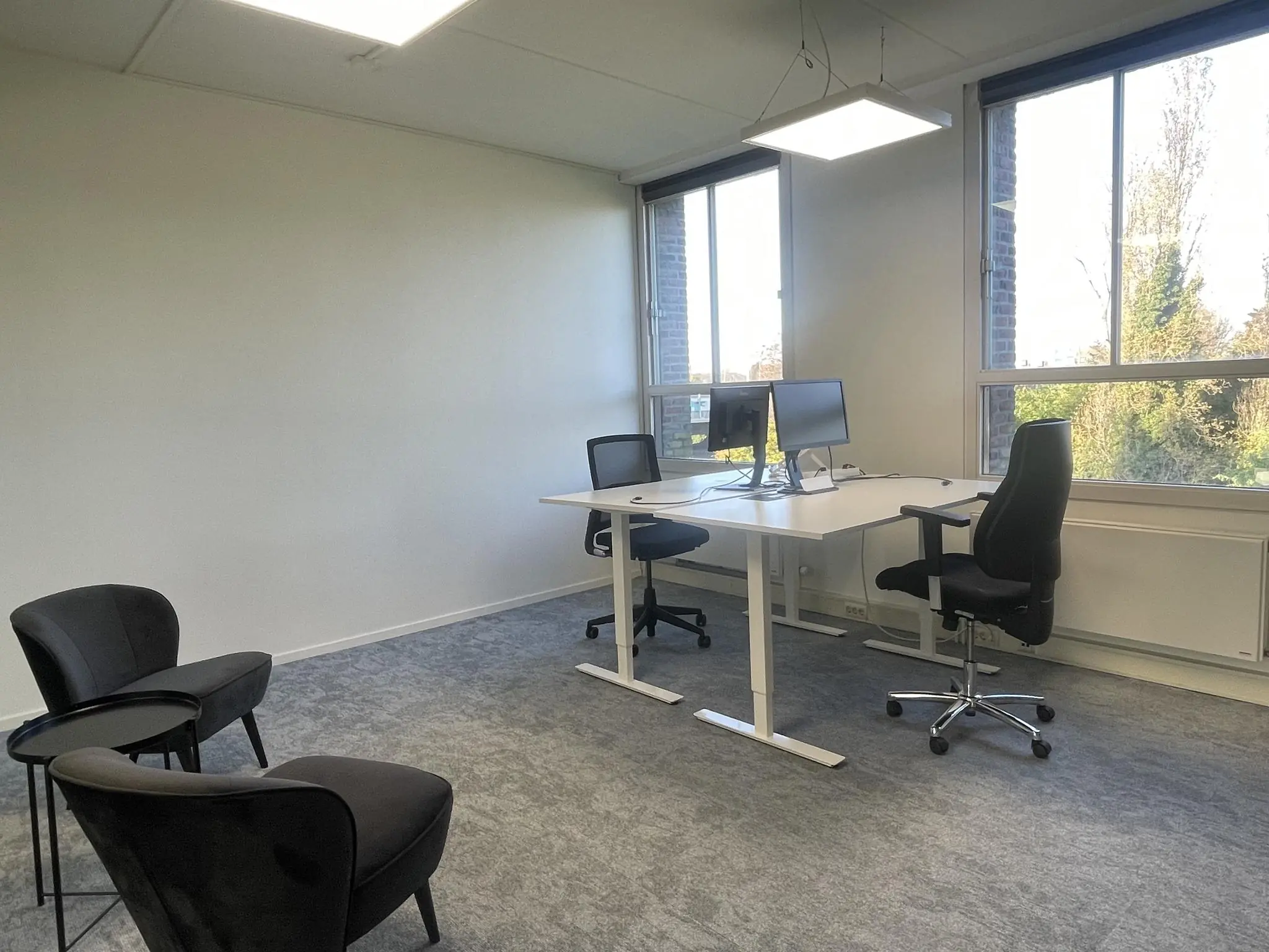 Modern ingericht kantoor aan de Jan Leentvaarlaan met bureaus, bureaustoelen, twee monitoren en zithoek met twee stoelen.